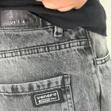 Pantalón de jean con corte ultra baggy, de tiro medio y diseño holgado en las piernas. Presenta un acabado lavado en tono gris oscuro y costuras reforzadas.
