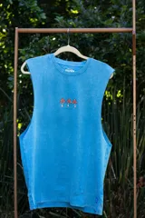 Musculosa sin mangas, color azul celeste con efecto acid wash, cuello redondo y amplias sisas. Presenta un pequeño estampado frontal de tres hongos rojos y blancos con la inscripción "Tuya" debajo.