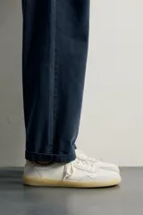 Zapatilla deportiva barefoot fabricada en piel, en color blanco con detalles en beige y gris, y suela de goma en contraste.
