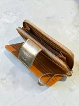 Billetera grande de cuero con acabado metalizado dorado y textura tipo reptil. Cuenta con un compartimento frontal con solapa y cierre a presión, decorado con el logo de la marca grabado.