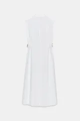 Vestido midi blanco, sin mangas, con cuello solapa y escote pico. Presenta falsos bolsillos con solapas en el pecho, trabillas con hebillas en la cintura y cierre frontal de botones.