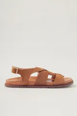 Sandalias planas de gamuza color suela con tiras cruzadas en el empeine y cierre con hebilla metálica dorada en el tobillo. Poseen plantilla de cuero y suela baja.
