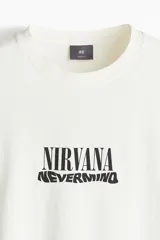 Remera color crema de corte holgado con estampado frontal del logo de la banda Nirvana y el título de su álbum Nevermind en color negro.