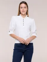 Buzo de algodón blanco con cuello mao y volados, manga tres cuartos abullonada y botones metálicos decorativos en la parte frontal.