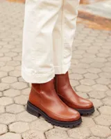Botas cortas de cuero color marrón con suela track negra de goma. Presentan un diseño de corte clásico con paneles laterales texturizados y cierre lateral interno.