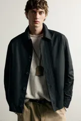 Sobrecamisa negra de corte relaxed fit, confeccionada en tejido de algodón con elasticidad. Cuenta con cuello solapa, manga larga con puño abotonado, bolsillos de vivo en la cadera y cierre frontal de botonadura.
