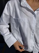 Camisa blanca de tejido texturado, corte oversize con mangas largas y puños anchos.