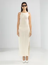 Vestido largo tejido color crudo, con cuello halter, espalda baja y abertura lateral.