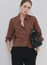 Camisa de poliéster color marrón con estampado de lunares blancos, cuello camisero, manga larga y cierre frontal de botones ocultos.