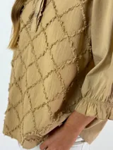 Blusa color beige con cuello mao, mangas 3/4 con puños elásticos y detalle de diseño geométrico texturizado en el frente.