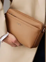 Bandolera Calvin Klein color tostado, con correa ancha de tela con logo de la marca y correa fina de cuero sintético.