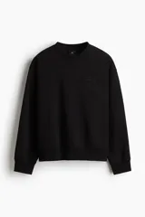 Buzo negro de tejido pesado con interior cepillado suave, cuello redondo y corte boxy. Presenta un diseño estampado en relieve tono sobre tono en el pecho.