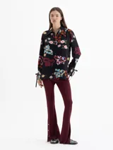 Camisa de seda color blanco con estampado floral y de dragones en tonos rojos, azules y verdes. Tiene cuello clásico, mangas largas con puños ajustables y botones forrados.