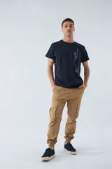 Pantalón cargo color beige, corte slim, con bolsillos laterales con botón, cierre con botón y puños en los tobillos.