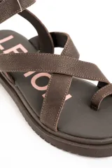 Sandalias planas de cuero marrón con tiras cruzadas, sujetadedos y tira con hebilla ajustable al tobillo.