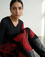 Vestido largo de corte fluido con escote en V y mangas largas. Presenta un diseño estampado con motivos de hojas en tonos rojos, terracota y borgoña sobre una base de color negro.