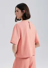 Blusa manga corta de tejido liso, color salmón, con cuello redondo y corte recto.