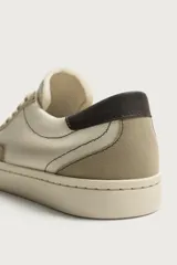 Zapatilla casual de tejido de algodón color beige con detalles en verde y un parche negro en el talón. Cuenta con suela de goma texturizada a contraste.