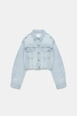 Campera de jean crop color celeste con efecto lavado, cuello solapa, mangas largas con hombreras, bolsillos con solapa en el pecho y detalles de rotos. Cuenta con cierre frontal de botones y bajo fruncido.