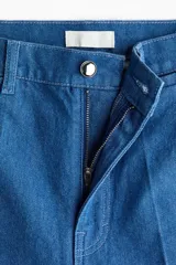 Jean de denim azul de tiro alto, con corte recto holgado, pliegues frontales y cierre con botón y cremallera.