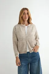 Campera tejida de punto con diseño a rayas horizontales en tonos beige y gris. Presenta cierre frontal completo, cuello redondo, bolsillos delanteros y puños y ruedo acanalados.