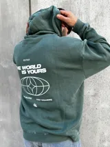 Canguro verde con capucha y cordones ajustables. Presenta un bolsillo tipo canguro y dos estampados blancos: un logo con forma de globo terráqueo en el lado izquierdo del pecho y una flor en el lado derecho.