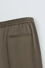 Pantalón regular fit color marrón oscuro, confeccionado en tejido con viscosa. Cuenta con cintura elástica, bolsillos delanteros y detalle de bolsillos traseros de vivo. El cierre frontal es con cremallera y botón.