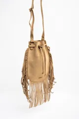 Cartera tipo bucket bag color camel, confeccionada en material sintético con acabado gamuzado. Presenta un diseño decorado con flecos largos en todo el contorno, cierre mediante cordón ajustable y correa larga regulable.