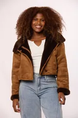 Campera corta tipo gamulán en color negro, con interior y detalles en puños y cuello de corderito sintético al tono. Presenta cierre frontal metálico y un botón decorativo en el ruedo.