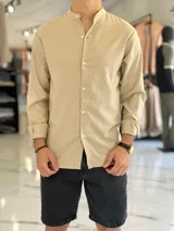 Camisa de lino color beige, de manga larga con puños arremangados y cuello mao. Cuenta con cierre frontal de botones y diseño clásico.