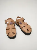 Sandalias de cuero marrón con tiras entrecruzadas, suela de goma negra con pespuntes blancos y hebilla lateral.