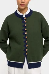 Saco tejido de punto en color verde, con cierre frontal mediante alamares y botones. Presenta detalles en contraste de color azul marino en el cuello, la botonera y el ruedo, este último con una línea blanca adicional.