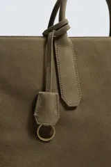 Bolso tipo bandolera de piel con acabado abatanado, diseño rectangular con doble asa de mano y detalle de llavero colgante. Cuenta con compartimento principal con cierre de mosquetón y bolsillo interior con cremallera.