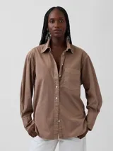 Camisa de corte oversize en color marrón, con cuello clásico, cierre frontal de botones, bolsillo en el pecho y mangas largas con puños anchos.