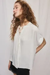 Camisa de manga corta color celeste, confeccionada en viscosa fluida, con silueta amplia y escote redondo con frunces y lazo para anudar.