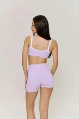 Conjunto deportivo compuesto por un top con breteles y un short de tiro alto, ambos en color lila con detalles en blanco. El top presenta un diseño con escote redondo y el short es de corte ajustado.
