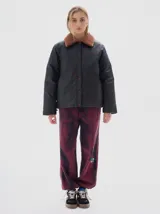 Campera verde con cuello de piel sintética blanca, cierre de botones a presión, bolsillos frontales y elástico en el dobladillo inferior. El forro interior es de algodón estampado.