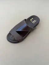 Sandalias de cuero color marrón con diseño asimétrico de tiras y plantilla anatómica. Tienen ajuste lateral con velcro y suela plana.