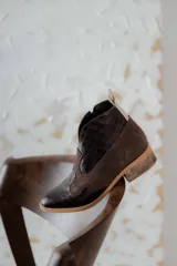 Botas cortas de estilo western confeccionadas en cuero, con puntera y talón texturizados con diseño de reptil y paneles laterales de gamuza. Presentan cierre lateral, tirador en la parte superior y taco bajo de madera.