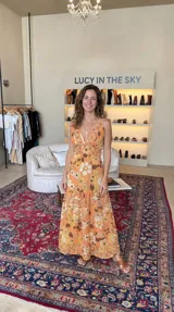 Maxivestido naranja con estampado floral en tonos amarillos, blancos y marrones, escote en V profundo, tirantes finos y cintura fruncida.