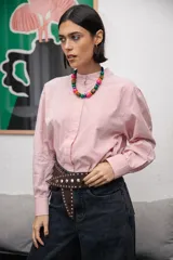 Camisa de corte clásico con cuello mao y cierre frontal oculto, confeccionada en tela de algodón con estampado de rayas verticales finas en color rojo y blanco. Presenta mangas largas con puños abotonados.