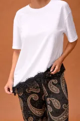 Remera blanca de corte clásico con cuello redondo y mangas cortas, que presenta un detalle asimétrico en el ruedo con encaje negro.