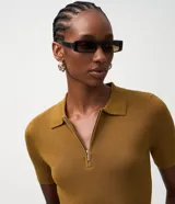 Blusa polo de punto color mostaza, ajustada al cuerpo, con cuello y manga corta. Presenta una cremallera frontal que llega hasta el escote.