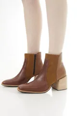 Botas cortas de cuero en tonos marrón y tostado, con diseño en paneles que combina cuero liso, gamuza y un sector con textura geométrica. Cuentan con taco ancho de madera, punta cuadrada y cierre lateral interno.