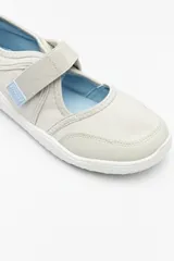 Zapatilla tipo guillermina de estilo barefoot, color beige con detalles en rosa pálido en el talón y tira de ajuste con velcro. Posee suela plana y flexible diseñada para un movimiento natural del pie.