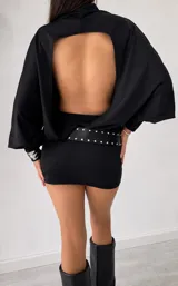 Vestido corto negro de cuello alto, con mangas largas abullonadas y puños ajustados. El diseño presenta un corte entallado en la falda y un estilo minimalista.