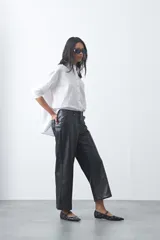 Pantalón de corte recto y pierna ancha confeccionado en cuero sintético negro, con acabado estructurado y tiro medio.