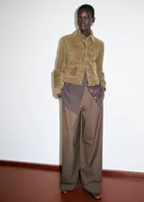 Chaqueta corta de piel de serraje color marrón, con diseño recto, cuello camisero, manga larga y cierre frontal de botones metálicos. Cuenta con dos bolsillos de parche con solapa en la parte delantera y forro interior.