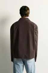 Sobrecamisa de corte regular fit en color marrón oscuro, confeccionada en tejido de algodón. Presenta cuello solapa, cierre frontal con botones, manga larga y tres bolsillos plastrón en el frente.