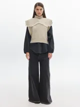 Chaleco de lana color beige con cuello alto y detalle de flecos en los hombros.